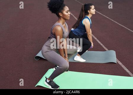 Deux amies font des squats avec des haltères à l'extérieur du stade. Banque D'Images
