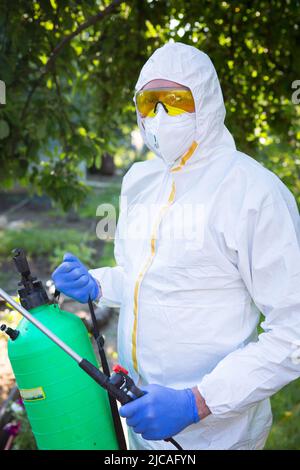 Le processus de traitement des plantes avec des pesticides. Un fermier dans un costume et un masque de protection tient un pollinisateur dans ses mains. Banque D'Images