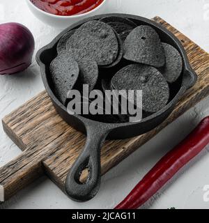 Ensemble de croustilles croustillantes noires, dans une poêle en fonte, sur une surface en pierre blanche Banque D'Images