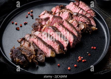 Tranches de bœuf grillé Rib eye steak de bœuf marbré rare, sur assiette, sur vieux fond rustique foncé Banque D'Images
