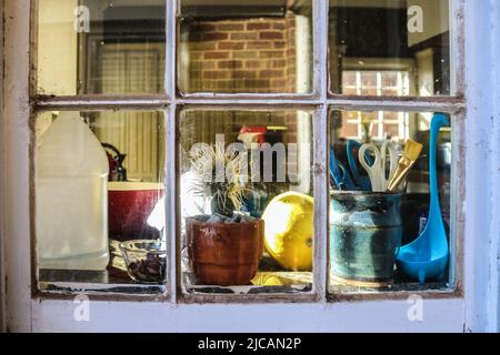 Piquer dans la fenêtre de la cuisine à travers la fenêtre sale avec le calfeutrage craquant et les spiderwebs au comptoir bondé avec des réflexions hors foyer - se concentrer sur FO Banque D'Images