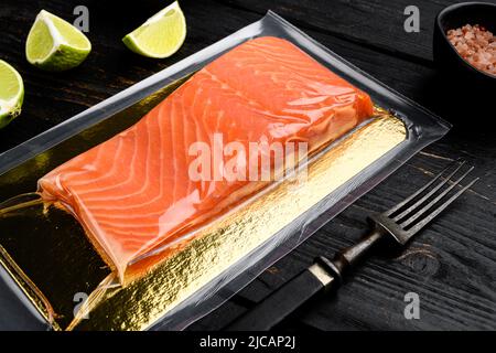 Filets de saumon dans un emballage sous vide, avec des herbes, sur fond de table en bois noir Banque D'Images