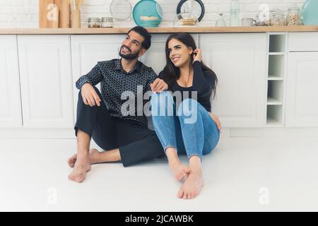 Joyeux interracial belle atractive newlyweds assis sur le sol de la cuisine et regardant vers le haut. Photo de haute qualité Banque D'Images