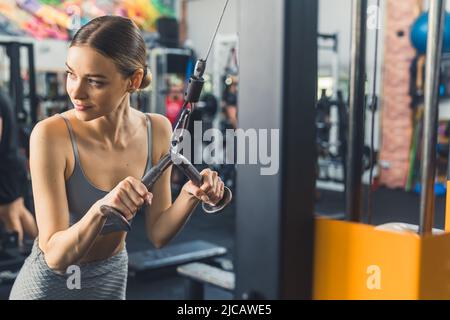Plan moyen d'une jolie femme attirante concentrée dans son 20s tenant sur une machine pour pomper les muscles de dos. Photo de haute qualité Banque D'Images