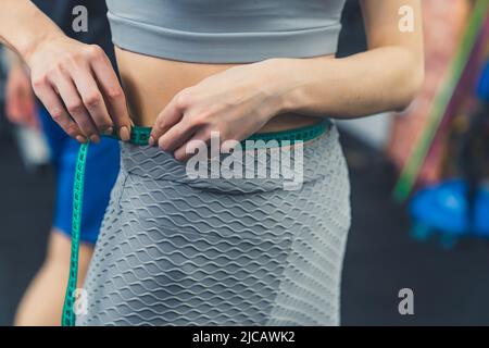 Gros plan en intérieur d'une femme mince de race blanche méconnaissable qui vérifie sa taille à l'aide d'un ruban de mesure. Mode de vie sain et concept de régime alimentaire. Photo de haute qualité Banque D'Images