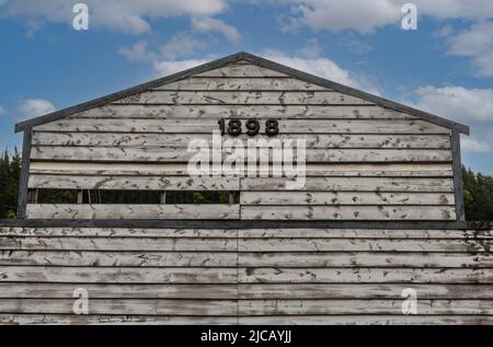 Skagway, Alaska, Etats-Unis - 20 juillet 2011: Gros plan de l'ancienne grange en bois gris au niveau supérieur avec date 1898 sous bleu ciel nuageux. Banque D'Images