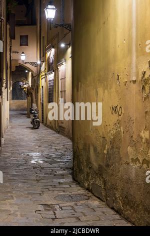 Une rue imprécise et longue éclairée par des lampadaires avec un scooter stationné et un panier à fleurs sur un mur Banque D'Images