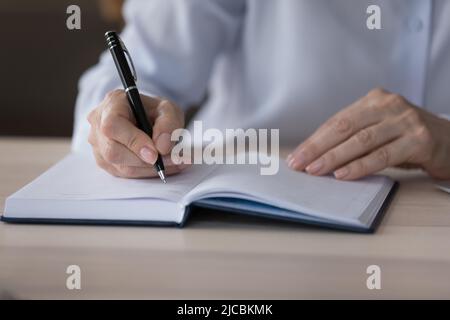 Gros plan une femme plus âgée tient les écritures de stylo dans un organiseur de papier personnel Banque D'Images