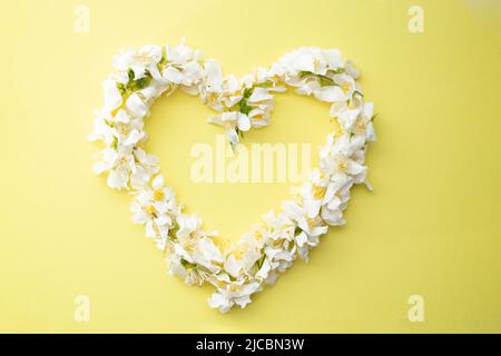 Petites fleurs blanches cadre en forme de coeur sur fond jaune. Maquette, modèle ou toile de fond romantique. Banque D'Images