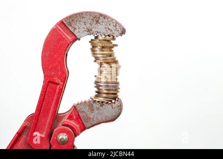 Clé à pipe pinçant une pile élevée de pièces, isolée sur fond blanc. Métaphore du coût de la plomberie. Banque D'Images