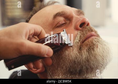 Un vieil homme enjoing coupe de cheveux par un maître dans un salon de coiffure. Un vieil homme obtient une coupe de cheveux élégante Banque D'Images