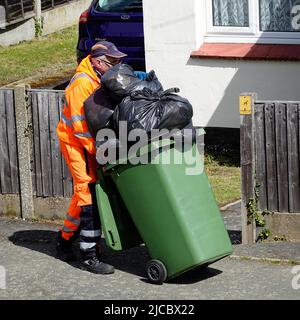 Gestion des déchets refuge collecteur poussière homme de travail haute visibilité vêtements poussant roue débordante poubelle pleine de sacs de déchets noirs Essex Angleterre Royaume-Uni Banque D'Images