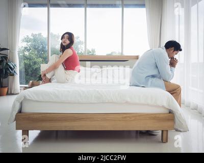 L'anxiété des amoureux du couple asiatique sur le lit. Homme et jeune femme attentionnés assis sur le lit avec des difficultés de relation se sentant triste et thinki Banque D'Images