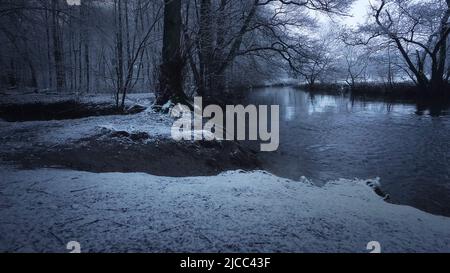 Neige légère dans la forêt par rivière en hiver crépuscule avec fonte bleue Banque D'Images