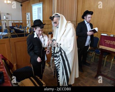 Quelques semaines avant sa cérémonie et sa célébration de Barmitzvah Menachem Mendel Pink est aidé à mettre le tephillim pour la première fois par son père Rabbi Yehuda Pink de la Solihull et de la Congrégation hébraïque de district dans les Midlands de l'Ouest et regardé par son grand-père M. Phaivish Pink, Directeur de l'école de grammaire juive de Manchester, lors d'un service le dimanche matin suivi d'un petit déjeuner de célébration pour sa famille et d'autres fidèles des communautés chasidiques de Lubavitch dans les West Midlands ainsi que des congrégants de la synagogue. Banque D'Images