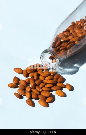 sur fond bleu, les amandes sont versées dans une bouteille de verre. le lait d'amande peut être un excellent substitut au lait de vache ordinaire. Banque D'Images