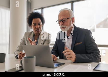 Une femme cadre discutant avec un professionnel senior sur un ordinateur portable. Les employés d'affaires planifient à leur bureau. Ils portent des coffrages au bureau. Banque D'Images