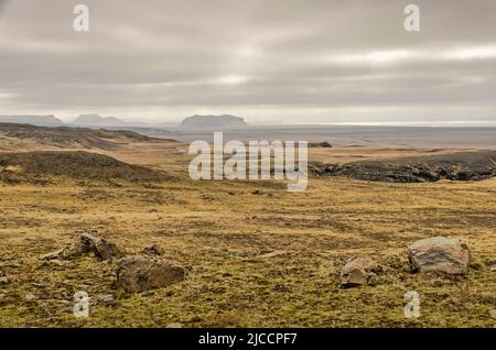 Plaine avec des rochers, de la mousse et de l'herbe dans les montagnes près de Skogar, Islande, avec une vue vers la côte sud, sous un ciel nuageux Banque D'Images