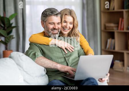 Technologies modernes. Joyeux conjoint d'âge moyen qui fait du temps avec un ordinateur portable à la maison Banque D'Images
