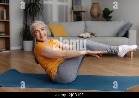 Bonne tenue femme senior faisant des exercices d'abs sur le tapis de yoga à la maison, l'exercice de ses muscles de noyau, faisant la forme physique domestique Banque D'Images