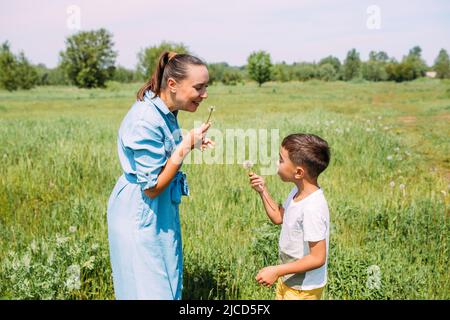 Les enfants d'âge préscolaire de maman et de fils passent du temps à l'extérieur en été et soufflent sur les pissenlits Banque D'Images