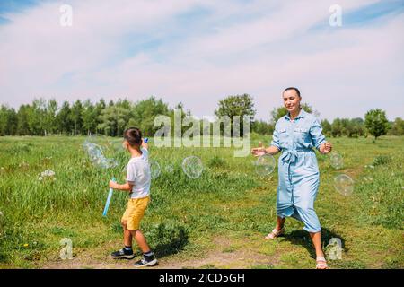 Les enfants d'âge préscolaire de maman et de fils passent du temps à l'extérieur en été et soufflent de grosses bulles de savon Banque D'Images