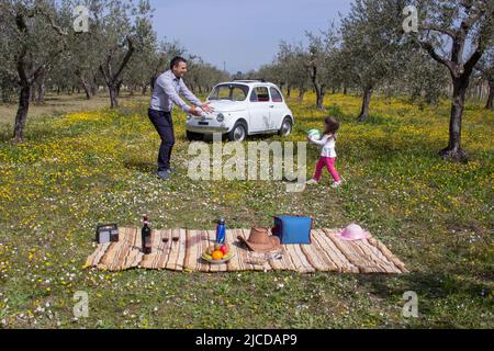 Image d'un père jouant au ballon avec sa fille pendant qu'ils ont un pique-nique pendant des vacances en Italie. Arrière-plan vieille voiture italienne dans un champ fleuri Banque D'Images