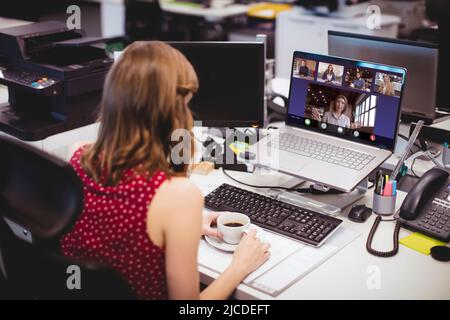 Femme d'affaires caucasienne avec une tasse de café sur le bureau, visioconférence avec des collègues sur ordinateur portable Banque D'Images