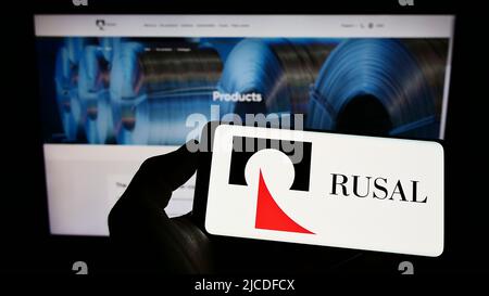 Personne tenant un téléphone portable avec le logo de la société russe United Company RUSAL IPJSC à l'écran en face de la page Web d'affaires. Mise au point sur l'affichage du téléphone. Banque D'Images