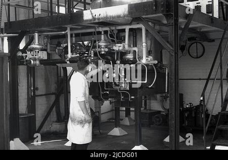 1960s, historique, une opérative masculine dans des combinaisons ajustant une valeur sur un tuyau dans une usine de fabrication de peinture, Angleterre, Royaume-Uni. À cette époque en Grande-Bretagne, plus de 1 000 petites entreprises fabriquaient de la peinture et des revêtements spécialisés, mais au fil du temps, ce nombre a été réduit à moins de cinquante au tournant du siècle. Banque D'Images