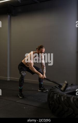 Pneu marteau de traîneau musclé roue homme frapper exercice force d'entraînement, concept équipement fort d'athlétisme de concentration de sportswear, homme Banque D'Images