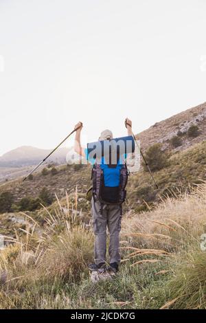 Photo verticale d'un randonneur, adulte, homme, caucasien, avec un sac à dos, tapis, poteaux, vêtu de t-shirt bleu, casquette et pantalon gris est sur les montagnes Banque D'Images