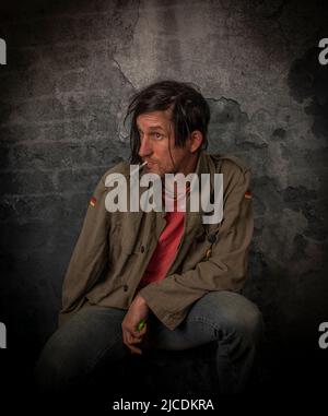 Junkie homme avec cheveux noirs et bouteille avec joint près de vieux mur de pierre Banque D'Images