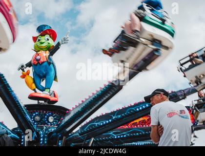 Homme assis devant le parcours de la foire de cricket de Jiminy au Morpeth Fair Day, le 2022 juin, à Northumberland Banque D'Images