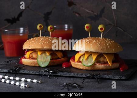 Deux burgers de poulet monstre drôle avec du pain grillé, du ketchup, des olives et du concombre. Cuisine créative d'Halloween Banque D'Images