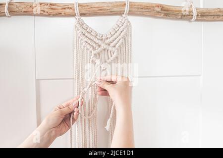 une fille tisse un motif macrame à partir de fils de coton blanc naturel pour un grand panneau mural Banque D'Images