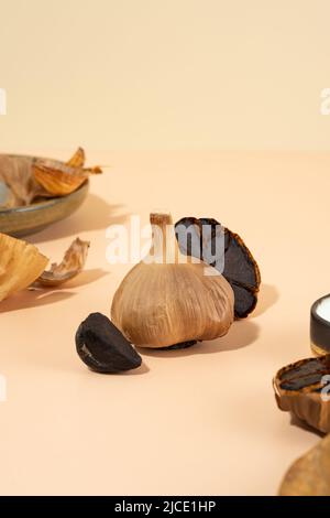 Une composition conceptuelle d'ail fermenté avec une ombre dure. Des bulbes et des gousses d'ail noirs sont situés sur un bureau beige. Nourriture saine, nourriture végétarienne Banque D'Images