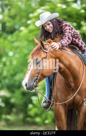 Une bonne fille rie et pante le cheval brun pendant une balade estivale dans la nature. Banque D'Images