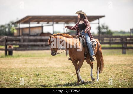 Une jeune cow-girl mène son cheval lors d'une promenade dans un ranch. Banque D'Images