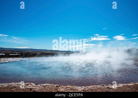 Fumée émise par le geyser de Strokkur au milieu du paysage contre le ciel bleu Banque D'Images