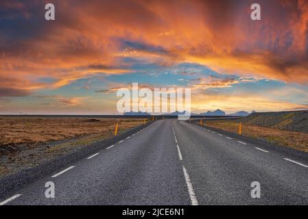 Diminution de la route vide au milieu du paysage volcanique contre ciel nuageux pendant le coucher du soleil Banque D'Images