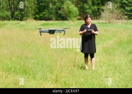 Jeune femme souriante pilote utilisant le drone par télécommande. Drone volant sur prairie . Une femelle lance un drone pour le vol. Banque D'Images