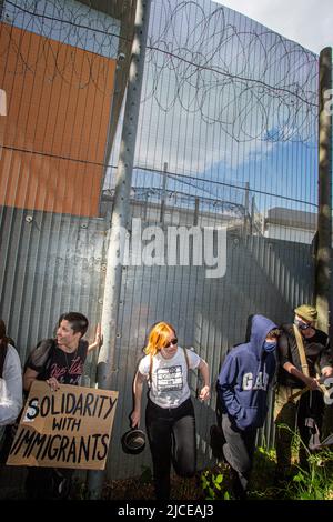 Les manifestants brandent et frappent contre l'escrime de périmètre contre les vols d'expulsion du Royaume-Uni vers le Rwanda à l'extérieur du centre d'enlèvement de l'immigration de Brook House. Banque D'Images