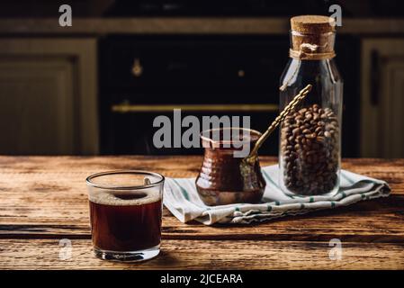 Café turc fraîchement préparé dans un verre à boire. Cezve et pot de grains de café rôtis. Banque D'Images