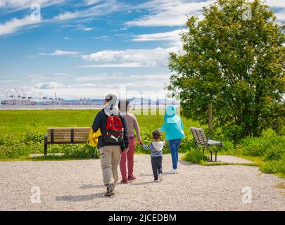 Famille avec enfants marchant dans le parc Spring par beau temps. Père et mère de famille asiatique tenant un petit enfant marchant et ayant du bon temps en somme Banque D'Images