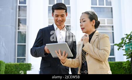 Femme d'affaires asiatique âgée ou entrepreneur discutant ou ayant un conseil informel avec un directeur financier professionnel masculin dans le parc de bureau. Banque D'Images