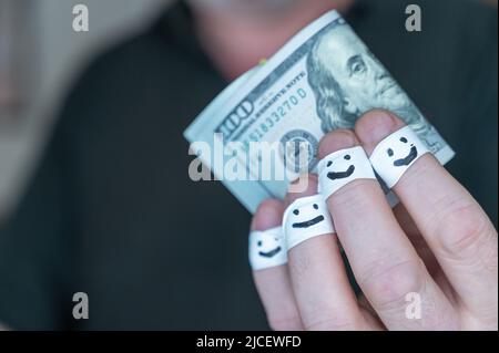 Un homme adulte tient sa main avec $100 billets à l'appareil photo. Les premières phalanges de ses doigts sont enveloppées dans un ruban blanc. Les visages souriants sont douloureux Banque D'Images