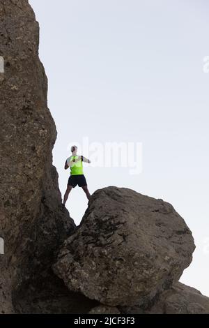 Touriste sur t-shirt jaune debout entre de grands rochers pour prendre des photos avec un smartphone. Jeune homme en randonnée jusqu'au bord de la falaise avec un téléphone portable entre les mains Banque D'Images