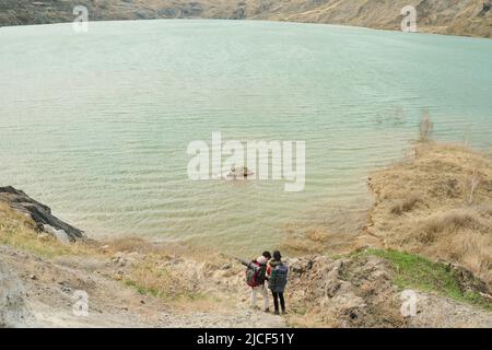Une photo extrêmement longue de deux touristes féminins non reconnaissables portant des sacs à dos debout sur la rive pittoresque du lac de carrière Banque D'Images