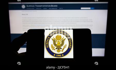 Personne tenant un smartphone portant le sceau de l'US surface Transportation Board (STB) à l'écran devant le site Web. Mise au point sur l'affichage du téléphone. Banque D'Images